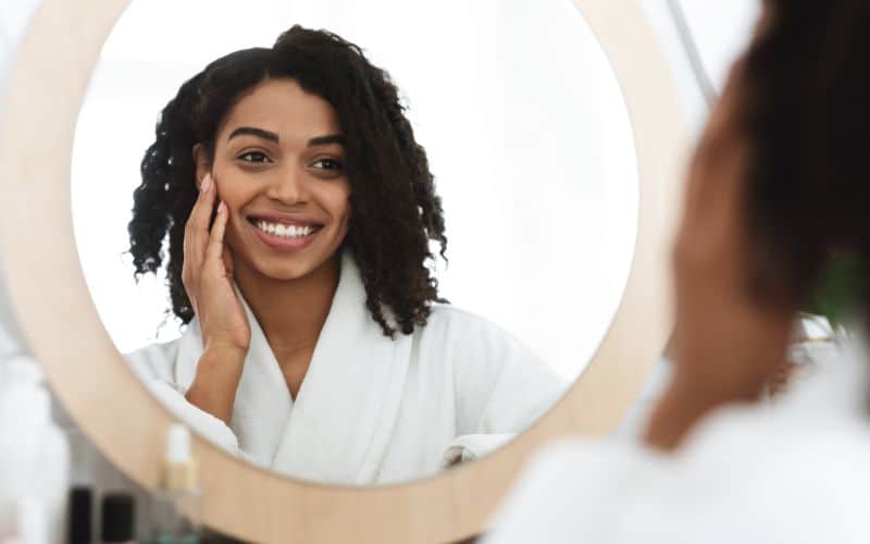 collagen-powder-happy-black-woman-touching-her-beautiful-face-while-looking-in-the-mirror-min